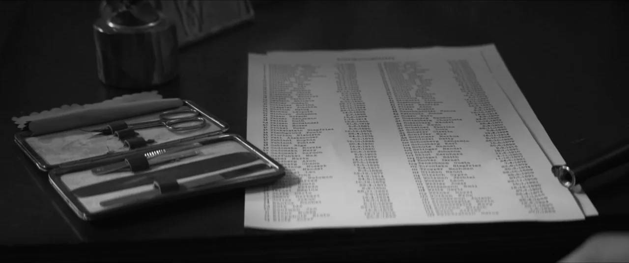 Bau, Artist at War (2025) movie still: closeup — A dark wooden desk holds a typed list of names and a grooming kit. The documents and small metal…