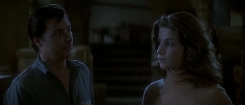 Assault on Precinct 13 (1976) movie still: medium — A dark indoor space with a dimly lit background containing indistinct furniture. A man and woman…
