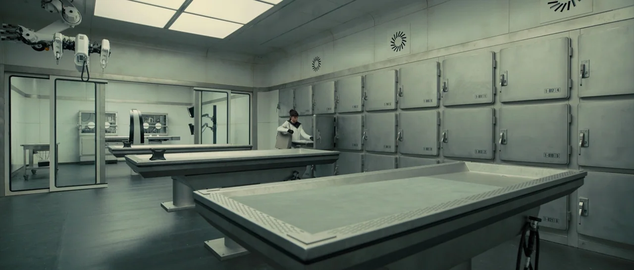 Blade Runner 2049 (2017) movie still: wide — A clinical morgue with rows of metallic storage cabinets and large stainless steel tables. A lone…