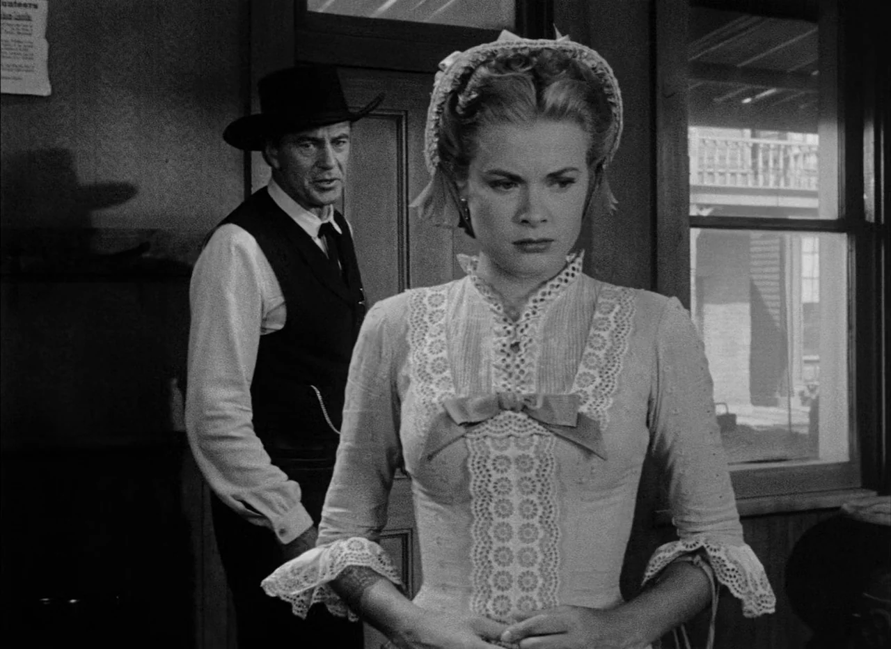 High Noon (1952) movie still: medium — An interior space features wooden door frames and a window viewing a wooden porch. A woman in a lacy dress…