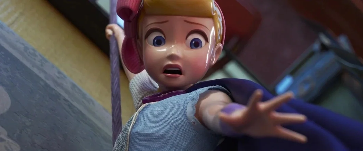Toy Story 4 (2019) movie still: closeup — A stylized toy figure hangs from a purple cord in a dimly lit room. She holds the rope with one hand while…