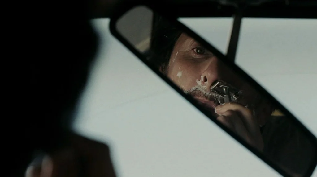 The Assassination of Richard Nixon (2004) movie still: closeup — A man's face is seen reflected in a car's rearview mirror. He is shaving his…
