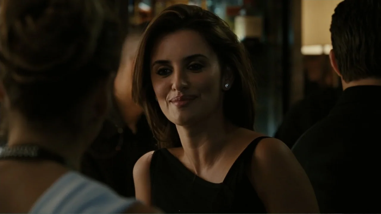 Sex and the City 2 (2010) movie still: medium — A dimly lit indoor space with blurred figures in the background. A woman in a black top turns her…