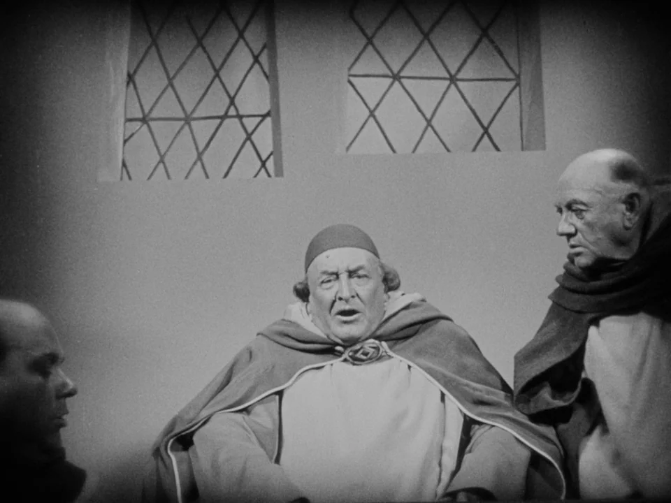 The Passion of Joan of Arc (1928) movie still: medium — A stone room with two diamond-paned windows features three men in clerical robes. The…