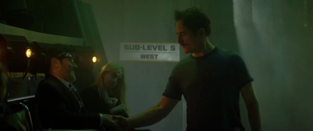 Officer Downe (2016) movie still: medium — An industrial hallway with a prominent sign reading SUB-LEVEL 5 WEST on the wall. A man in a t-shirt…