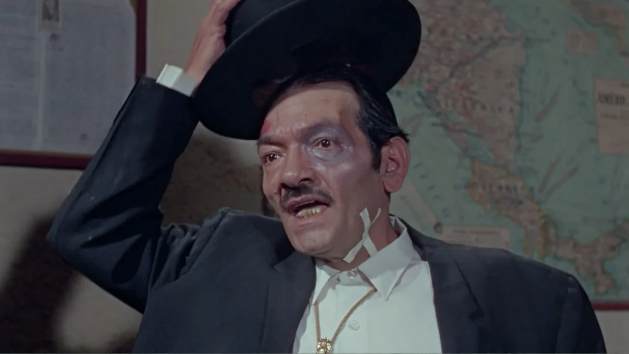 Los Dos Rivales (1966) movie still: medium — An interior office space features a map on the wall behind the subject. A man in a suit adjusts his hat…