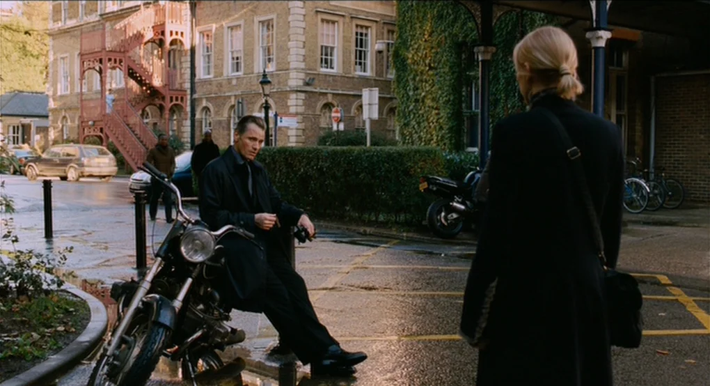 Eastern Promises (2007) movie still: medium — An urban courtyard with wet asphalt and red brick multi-story buildings in the background. A man leans…