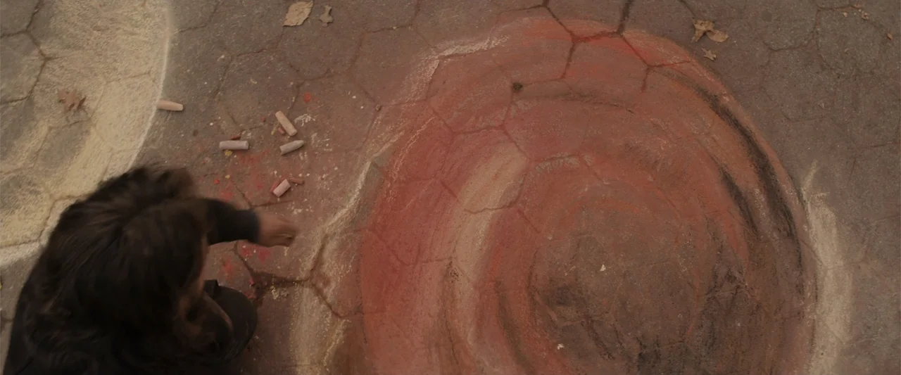 Winter's Tale (2014) movie still: medium — A concrete surface features a large circular chalk drawing with a spiral pattern. A person kneels on the…