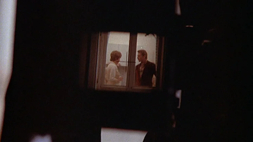 Day for Night (1973) movie still: wide — A man and a woman stand inside a brightly lit room viewed through a window. The surrounding area outside…