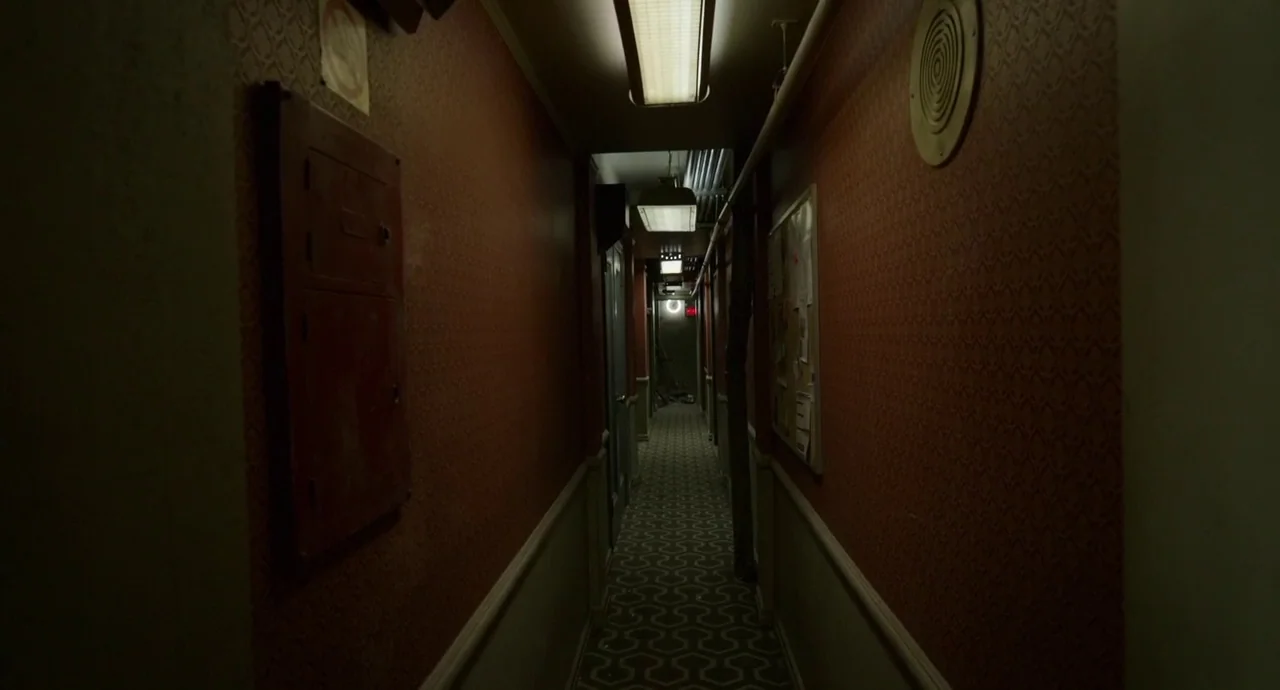 Birdman (2014) movie still: establishing — A long, dimly lit indoor hallway features patterned wallpaper and a geometric carpet. The narrow passage…