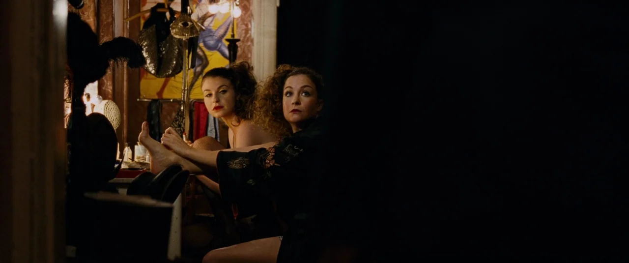 Phoenix (2014) movie still: medium — A cluttered theatrical dressing room contains vintage costumes and posters on the back walls. Two women sit at…