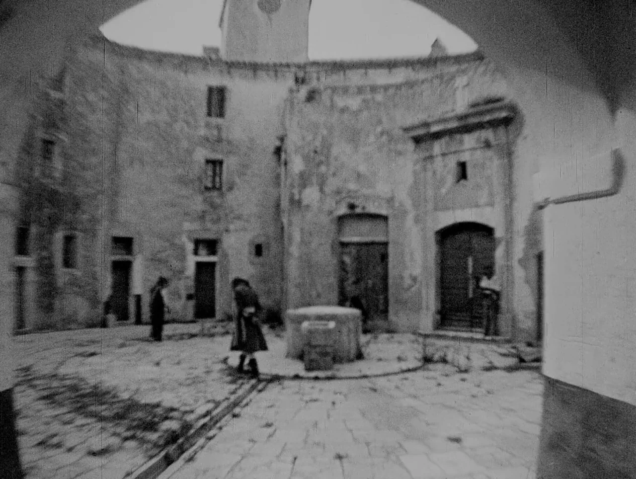Napoleon (1927) movie still: wide — An enclosed stone courtyard with arched entryways and weathered masonry walls. A central stone well sits on the…
