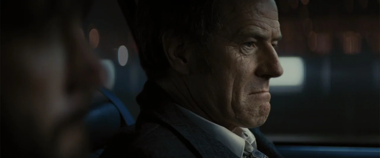 Argo (2012) movie still: medium — The interior of a moving vehicle at night with blurred city lights outside. An elderly man in a suit looks forward…