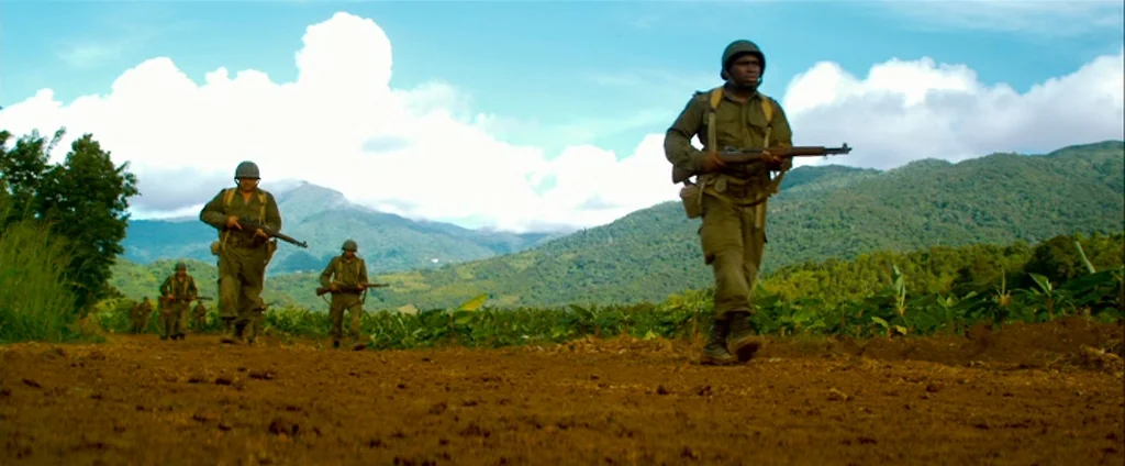 Che Part 1 (The Argentine) (2008) movie still: fullbody — A group of soldiers in olive uniforms march along a dirt road in a field. Large mountains…