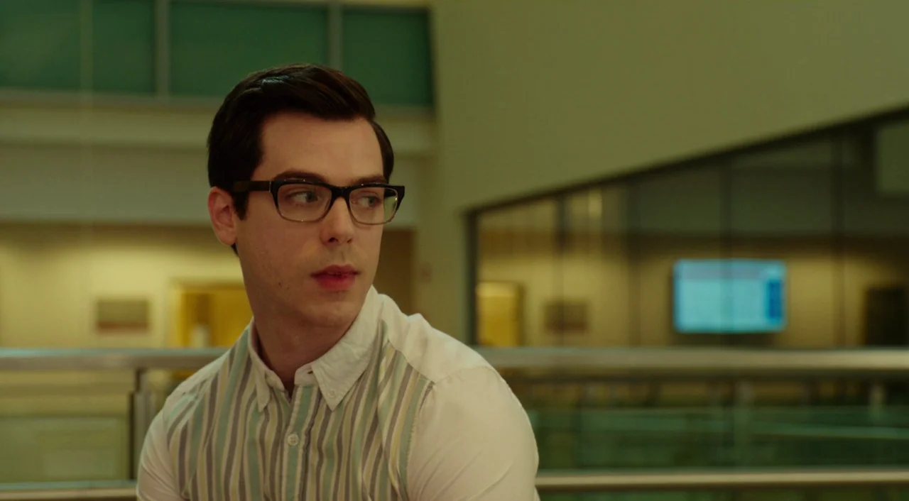 Wiener-Dog (2016) movie still: medium — A man stands inside a modern airport terminal with glass railings and blurred signage. He is looking off to…
