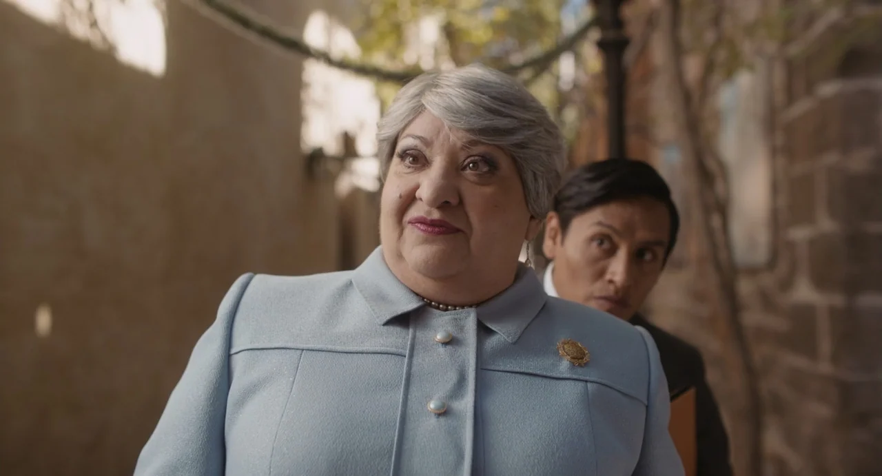 Dating Santa (2023) movie still: medium — An outdoor stone courtyard features weathered masonry walls and climbing vines in the background. An older…