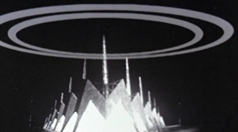 The Saddest Music in the World (2003) movie still: establishing — An alien spacecraft with triangular fins and double glowing rings hovers in…