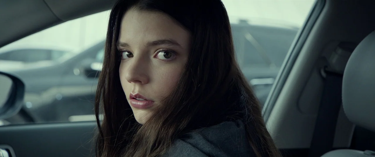 Split (2016) movie still: closeup — A close-up view inside a vehicle with gray interior paneling visible. A young woman with long dark hair looks…
