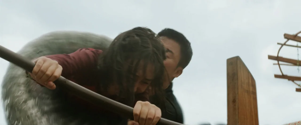 Meg 2: The Trench (2023) movie still: medium — An overcast sky overlooks a wooden boat on a river with blurred movement. A man and a woman grip a…