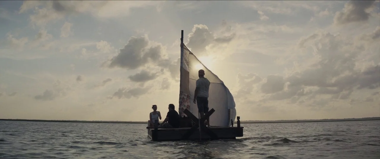 The Peanut Butter Falcon (2019) movie still: wide — Three people occupy a makeshift raft with a patchwork sail in open water. The group travels…