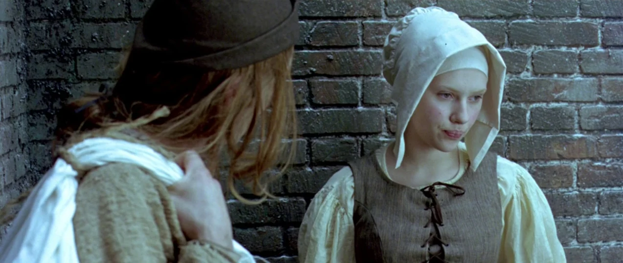 Girl with a Pearl Earring (2003) movie still: medium — A narrow alleyway features dark, weathered brick walls as the backdrop for two women. One…