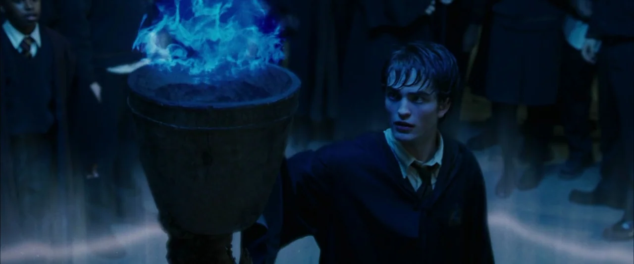 Harry Potter and the Goblet of Fire (2005) movie still: medium — A stone hall filled with students stands in dim, blue-lit surroundings. A young man…