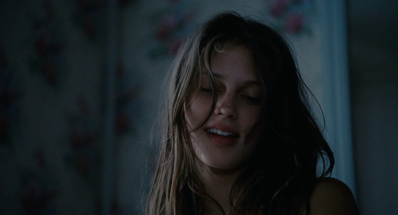Young & Beautiful (2013) movie still: closeup — A dimly lit room provides a dark, unfocused background behind a young woman. The woman has her eyes…