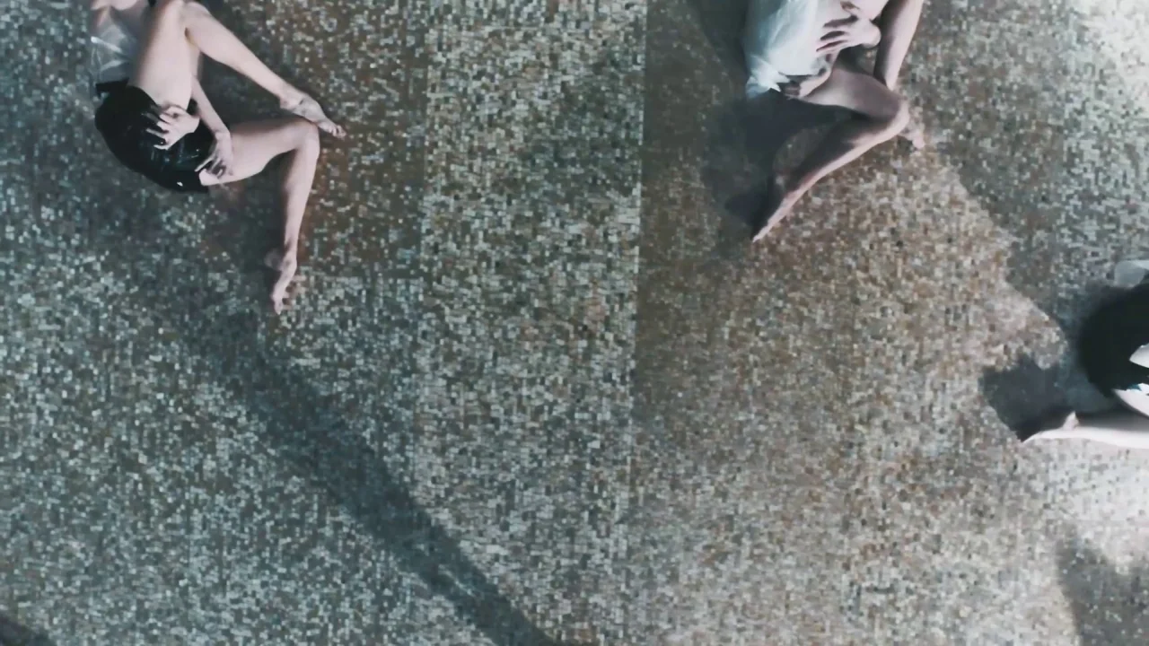 Collective: Unconscious (2016) movie still: wide — A top-down view shows three figures lying on a patterned mosaic-tiled surface. The individuals…