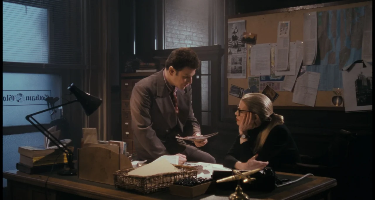 Batman (1989) movie still: medium — A cluttered 1940s-style newspaper office features a large desk with papers and a corkboard. A man in a suit…
