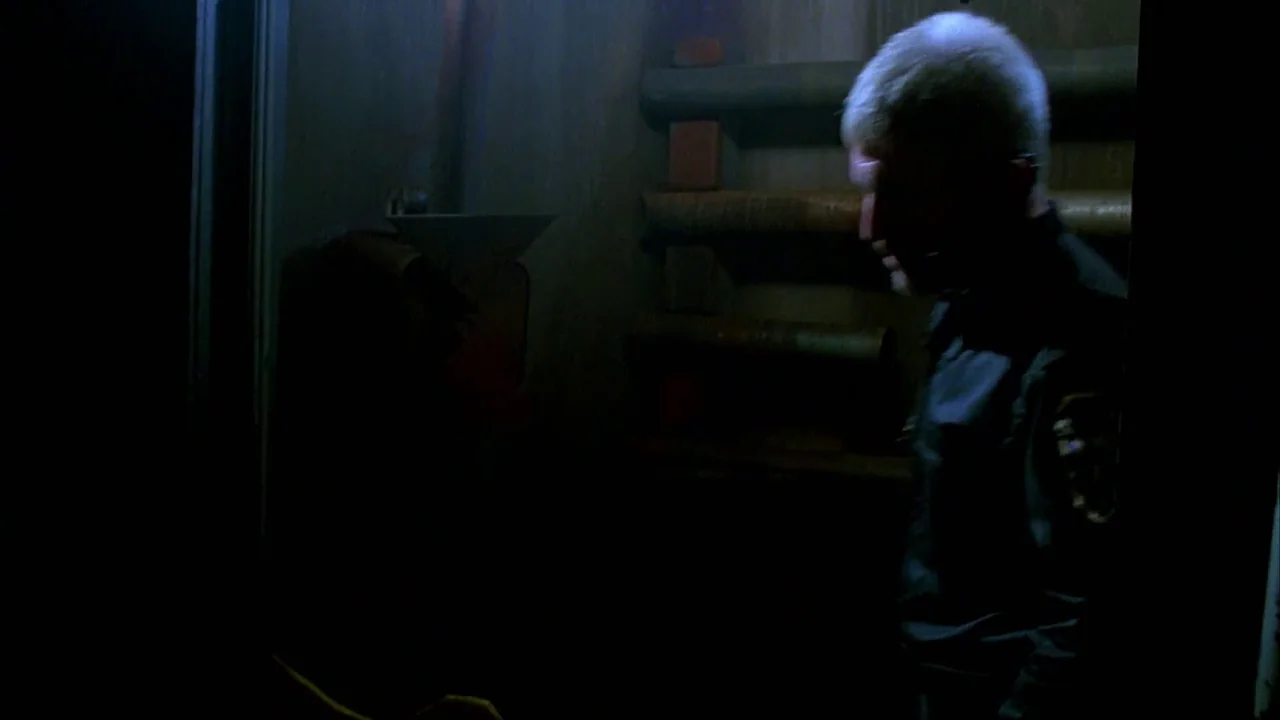 Hellraiser: Bloodline (1996) movie still: medium — A dimly lit industrial space features thick pipes mounted on a wooden wall. A man in a dark…