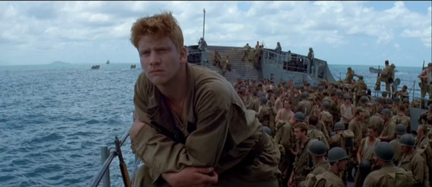 The Thin Red Line movie still: medium — A crowded transport ship deck at sea under a daytime sky with clouds. A young soldier with red hair leans…