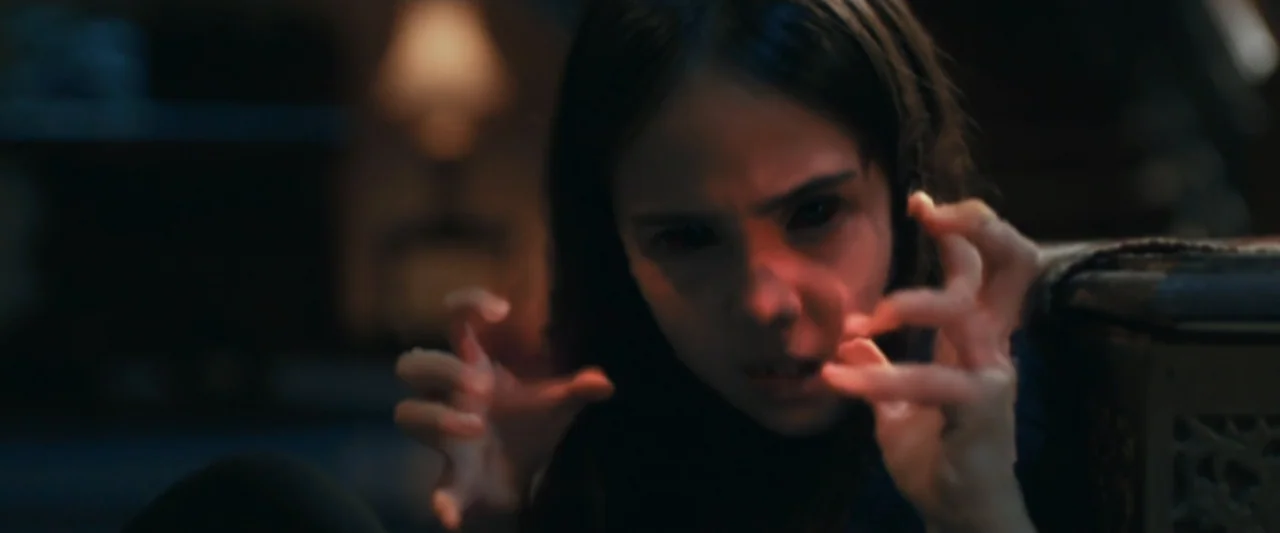 The Chanting 3 (2008) movie still: closeup — A dark indoor space with a dim light source in the background. A young girl with black eyes holds her…