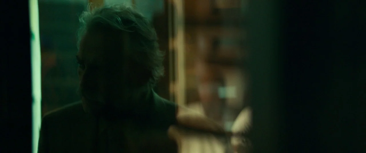 Halloween (2018) (2018) movie still: closeup — An interior space is shrouded in deep shadows and a cool green light source. An older man stands in…