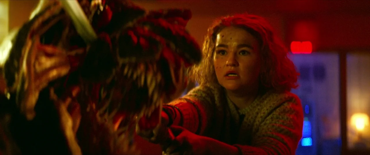 A Quiet Place Part II (2020) movie still: medium — A dark retail environment is illuminated by intense glowing red neon signs. A young woman in a…