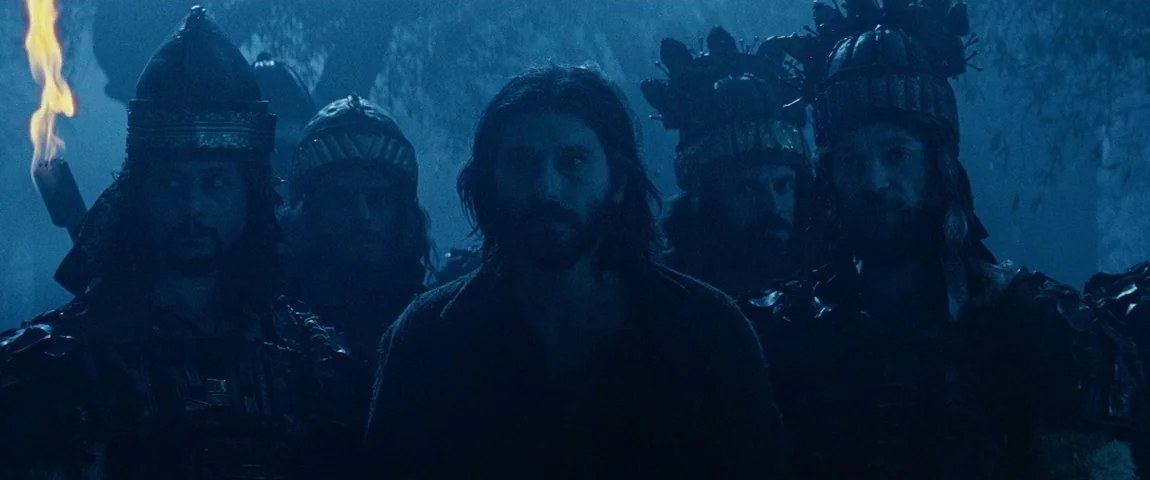 The Passion of the Christ (2004) movie still: medium — An ancient grove at night is illuminated by cold blue moonlight and a torch. A man with long…