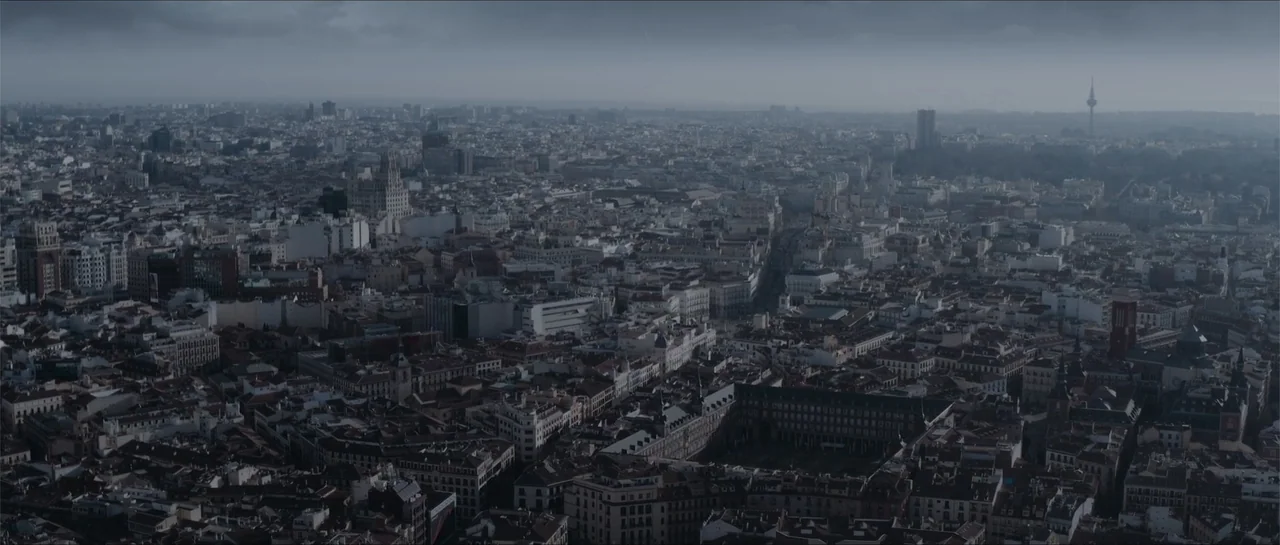 Historias lamentables (2021) movie still: establishing — A dense, expansive urban cityscape stretches to the horizon under a cloudy gray sky.…