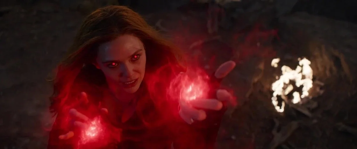 Avengers: Endgame (2019) movie still: closeup — A dark, rubble-filled exterior landscape lit by distant flames and magical red energy. A young woman…