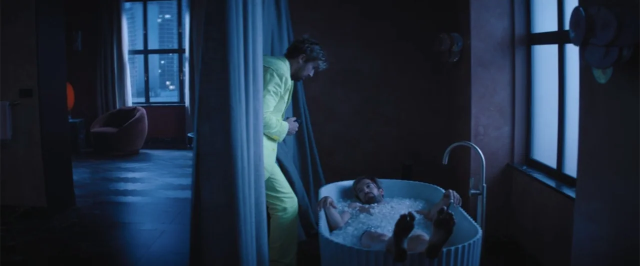 The Fall Guy (2024) movie still: medium — A dark, modern hotel bathroom features a free-standing tub filled with clear ice cubes. One man in a…