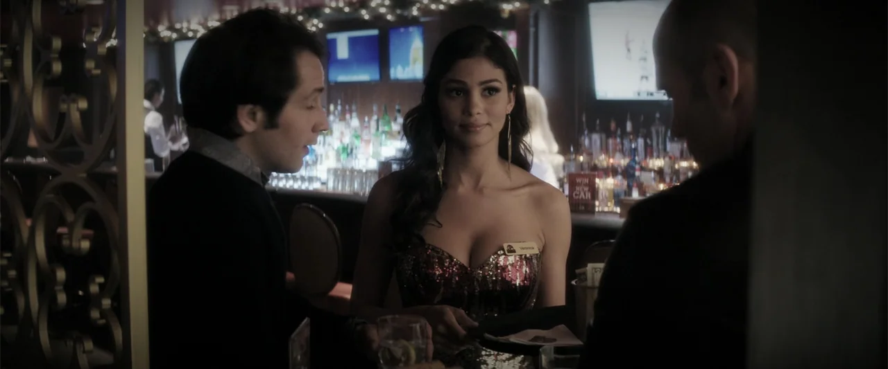 Wild Card (2015) movie still: medium — A dimly lit bar interior featuring a back counter with bottles and multiple televisions. A woman wearing a…