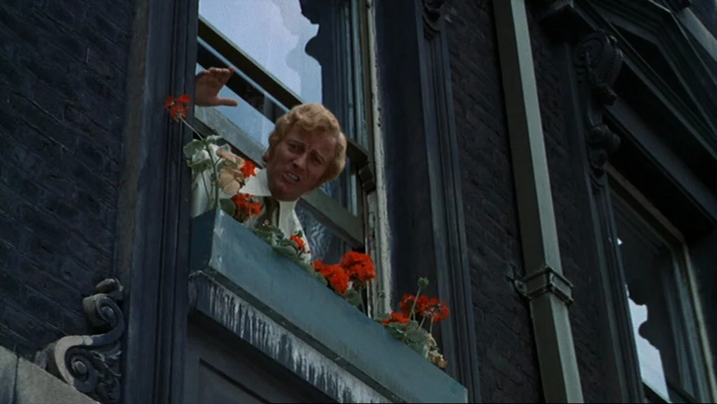 Frenzy (1972) movie still: medium — A dark brick building facade features a window with an external planter box. A man leans out from the open…