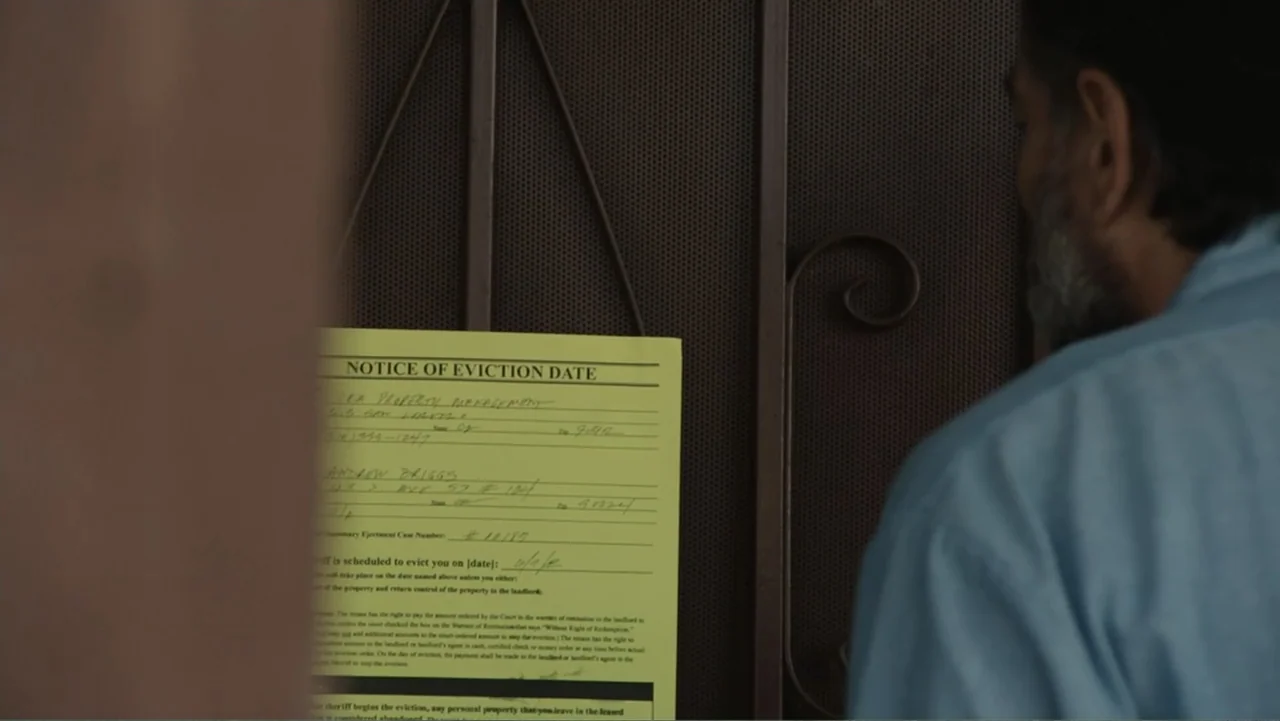 The Cleaner (2021) movie still: medium — A man stands before a metal security door with a yellow eviction notice attached. The man looks closely at…