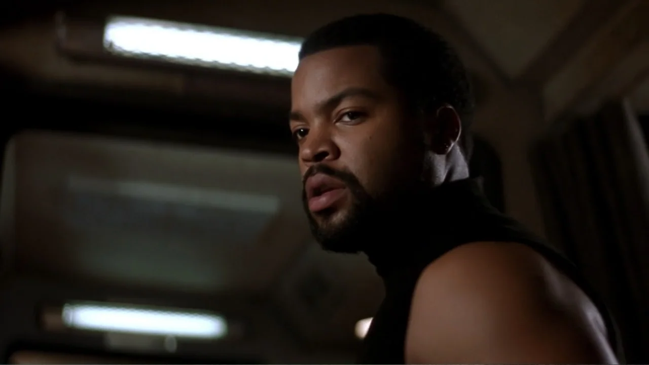 Ghosts of Mars (2001) movie still: closeup — An interior cabin space with recessed overhead lighting fixtures blurred in the dark background. A…