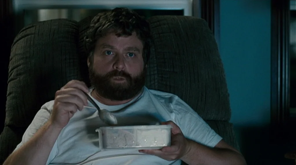Visioneers (2008) movie still: medium — A dimly lit space features a man sitting in a dark, textured upholstered armchair. He holds a plastic…
