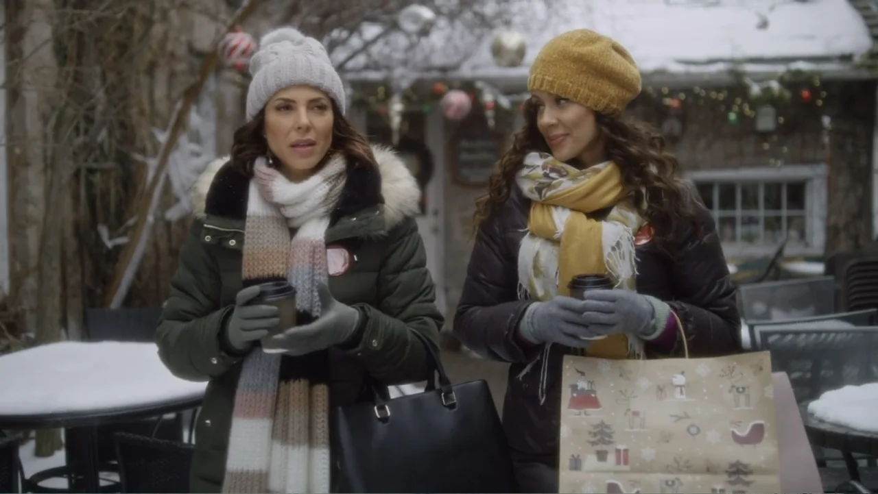 A Christmas Break (2020) movie still: medium — A snowy outdoor patio area decorated for the winter holidays with scattered furniture. Two women walk…