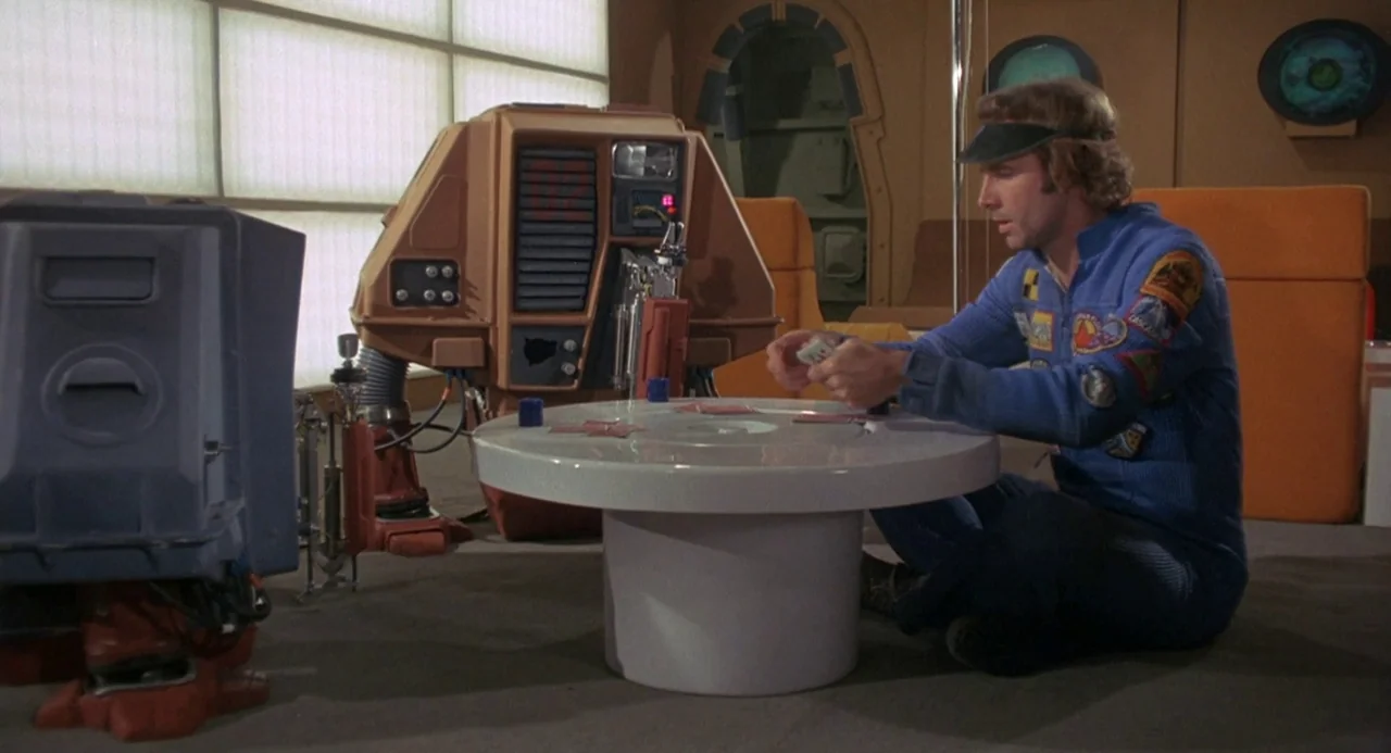 Silent Running (1972) movie still: medium — A futuristic crew lounge contains orange furniture and beige wall panels with geometric windows. A man…