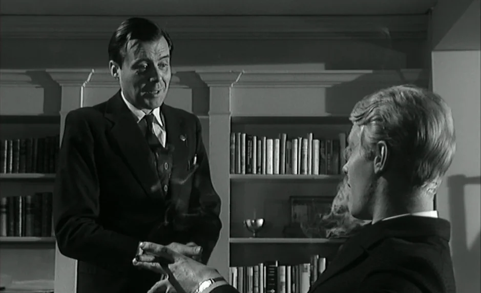 The Servant (1963) movie still: medium — A dark, wood-paneled room features floor-to-ceiling shelving filled with numerous hardback books. A man in…