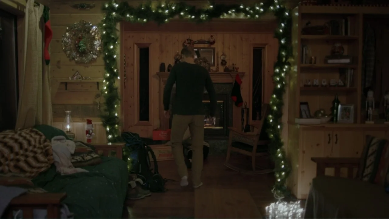 Alex & Emma (2003) movie still: fullbody — A rustic cabin living room decorated for Christmas with a large garland and lights. A man stands in the…