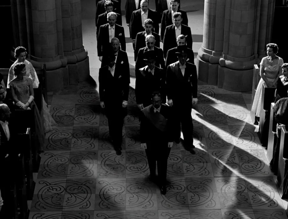 Wild Strawberries (1957) movie still: wide — A stone floor with decorative tile patterns lies between two large stone pillars. Several men in formal…
