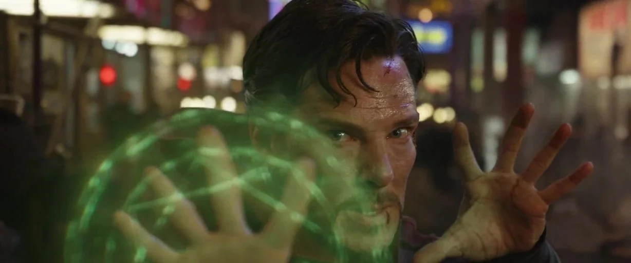 Doctor Strange (2016) movie still: closeup — A man stands in an out-of-focus city environment illuminated by night lights. He holds a bright green…