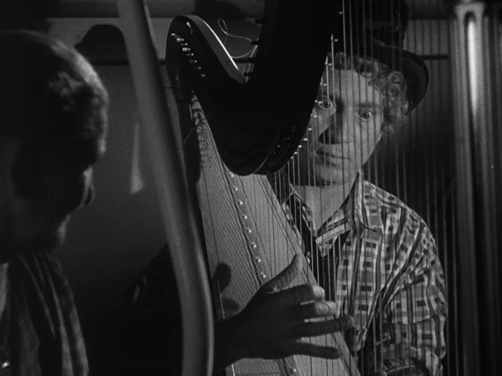 A Night at the Opera (1935) movie still: medium — A man in a top hat plays a large harp in a dimly lit room. He looks directly through the…